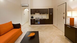 A compact living space with a kitchenette, a sofa, a coffee table, and a lamp. - Apartment with beautiful sea view (Santa Teresa Gallura)