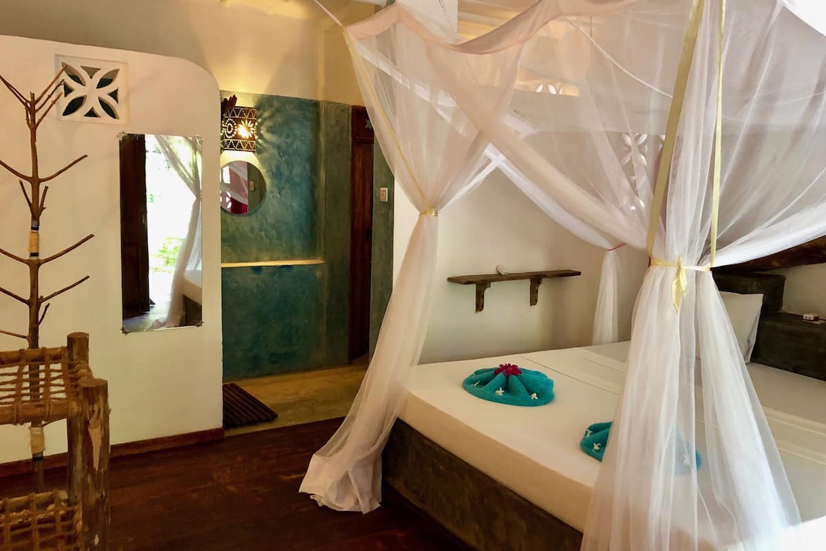 A bedroom with a canopy bed, a small round mirror, and a decorative tree.