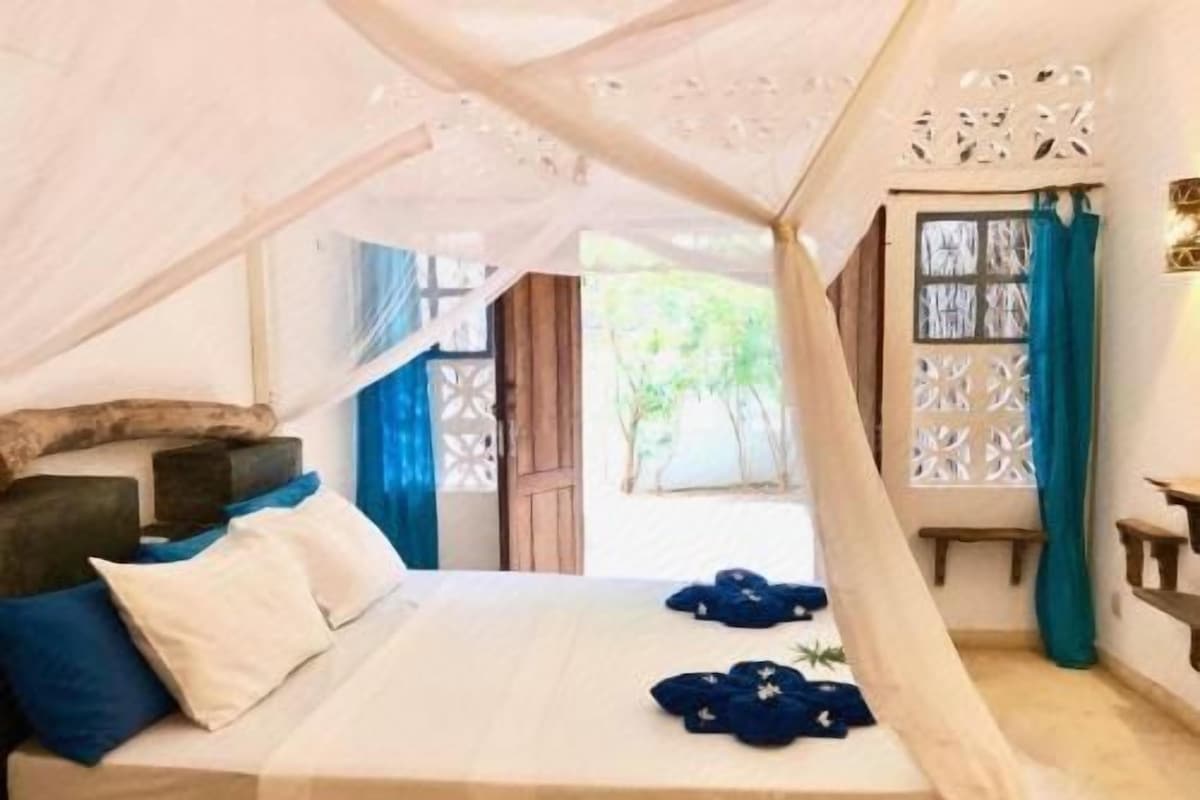 A bedroom with a bed, a canopy, a window with curtains, and a view of greenery outside.