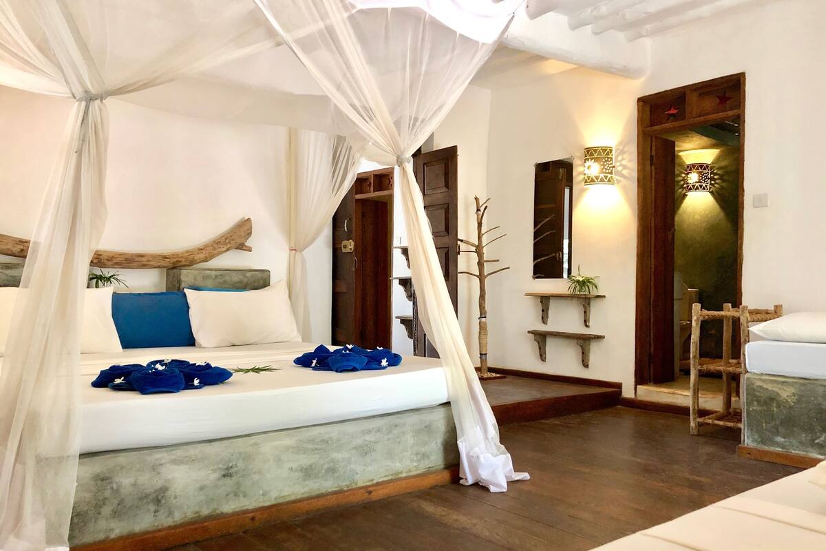 A room with a bed, a wooden headboard, a nightstand, a chair, a mirror, and a wall-mounted shelf with a plant.