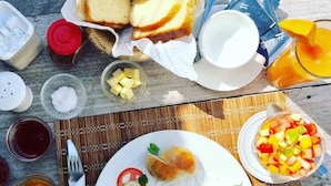 Desayuno con huevos, tostadas, fruta y bebidas sobre una mesa de madera.
