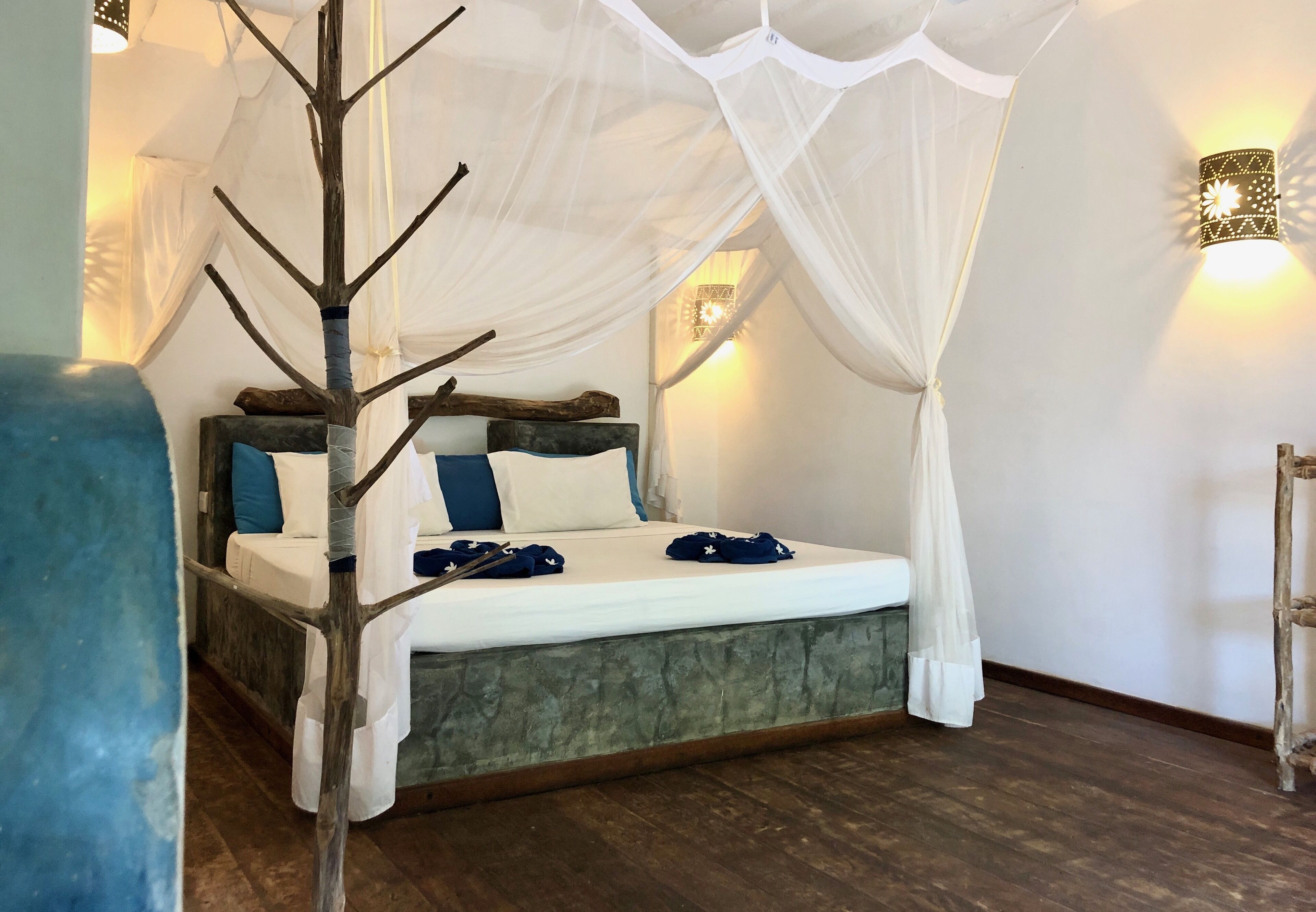 A bedroom with a canopy bed, a nightstand, and a wall-mounted lamp.
