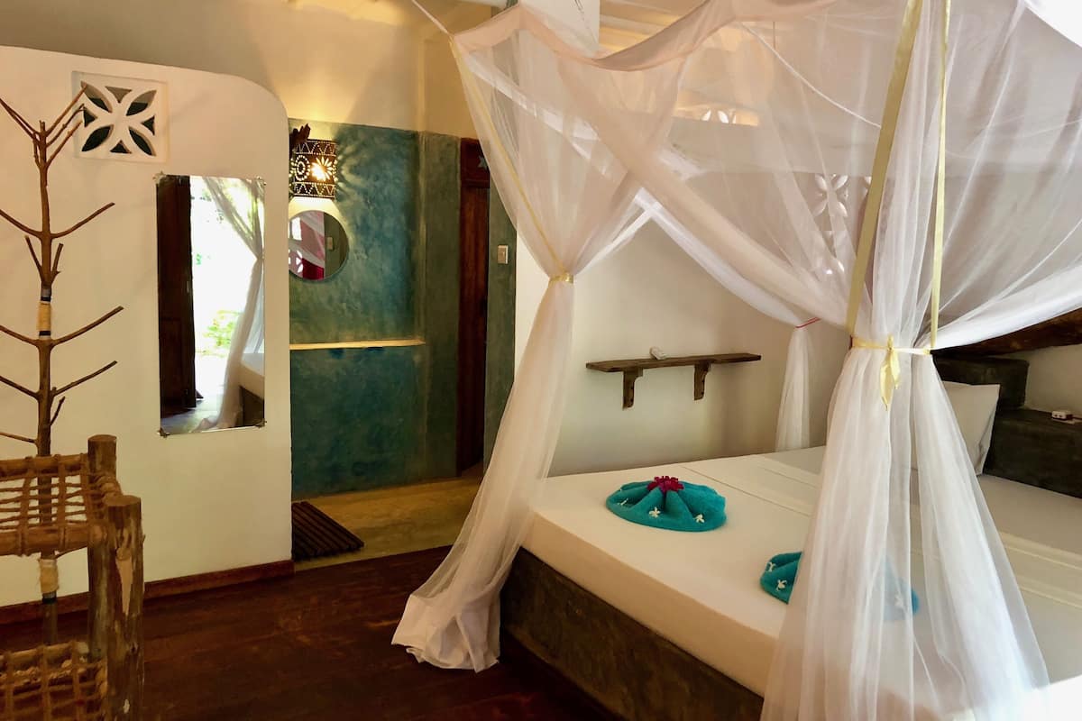 A bedroom with a canopy bed, a small round mirror, and a decorative tree.
