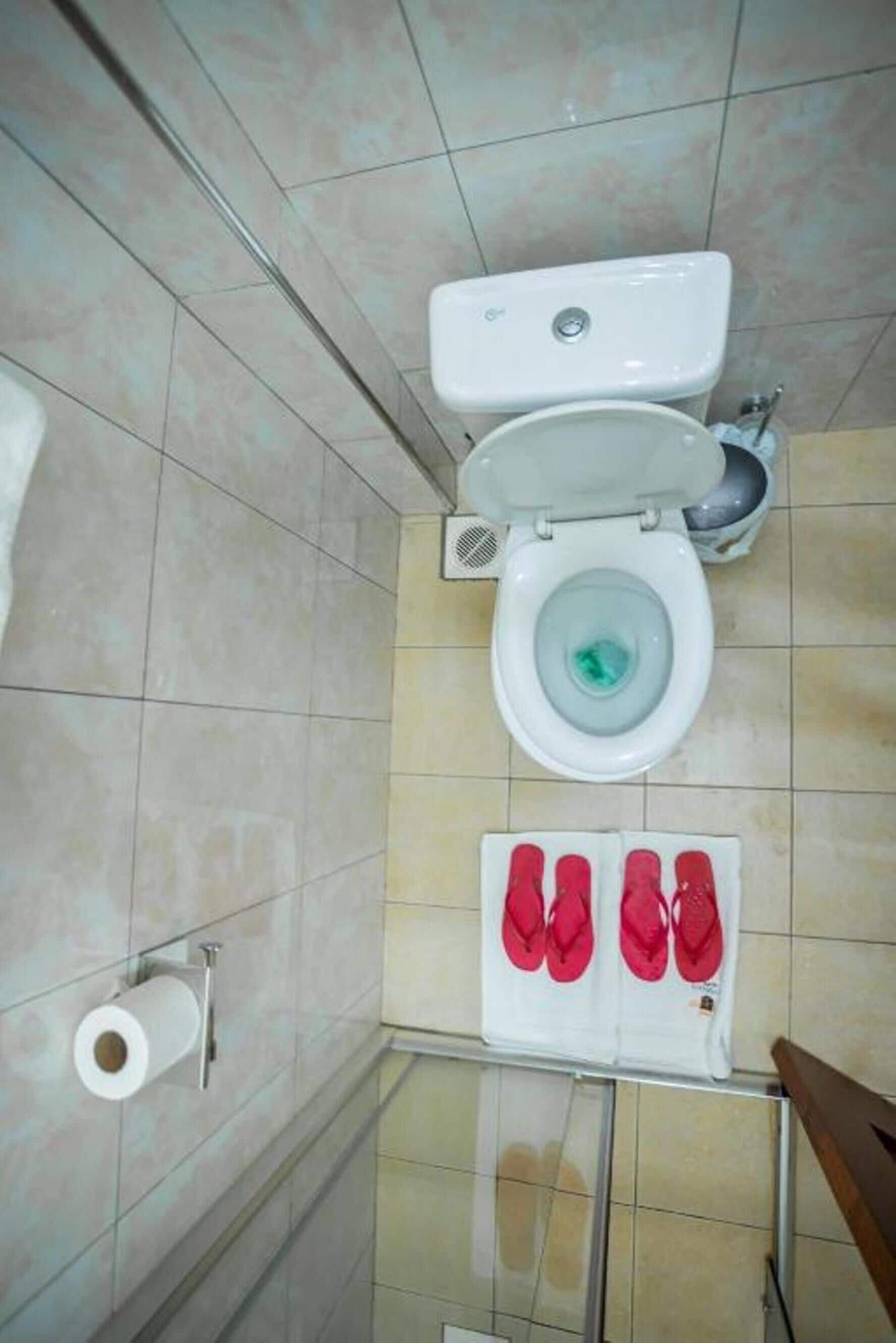 A bathroom with a toilet, a sink, and a pair of red slippers on a rack.