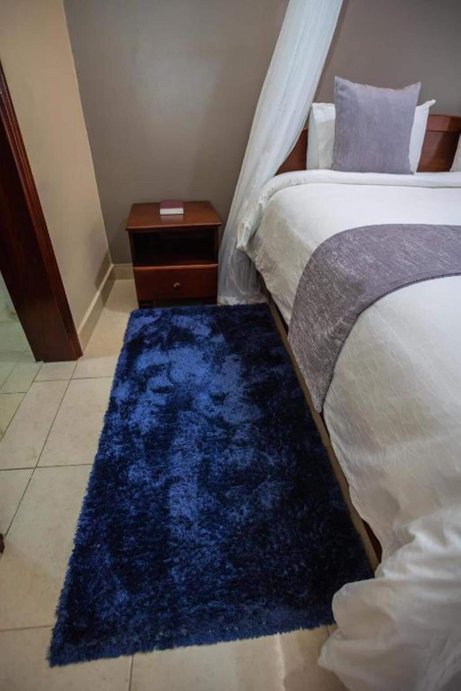 Une chambre à coucher avec un lit, une table de chevet, un tapis bleu et un baldaquin blanc.