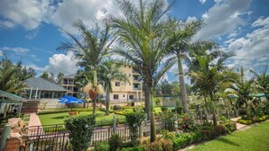 Un hotel con un jardín bien cuidado, palmeras y un cielo azul despejado.