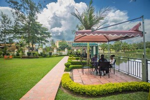 Un patio con zona de estar techada, un camino y un cuerpo de agua.