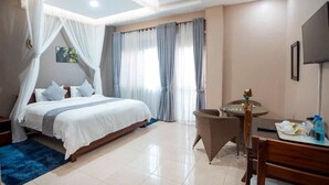 Un dormitorio con una cama, una mesita con una silla, un televisor y una ventana con cortinas.
