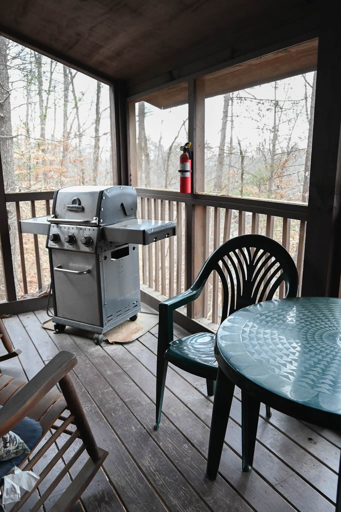 Een overdekt buitengebied met een barbecue, een tafel en stoelen.