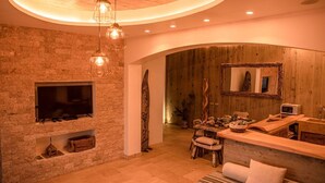 A cozy room with a stone wall, a fireplace, a wooden ceiling, and a dining area with a table and chairs. - Villa in Nature (Vila do Porto)
