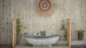 A stone bathtub in a spa setting with bamboo plants and a woven wall art piece. - Villa in Nature (Vila do Porto)