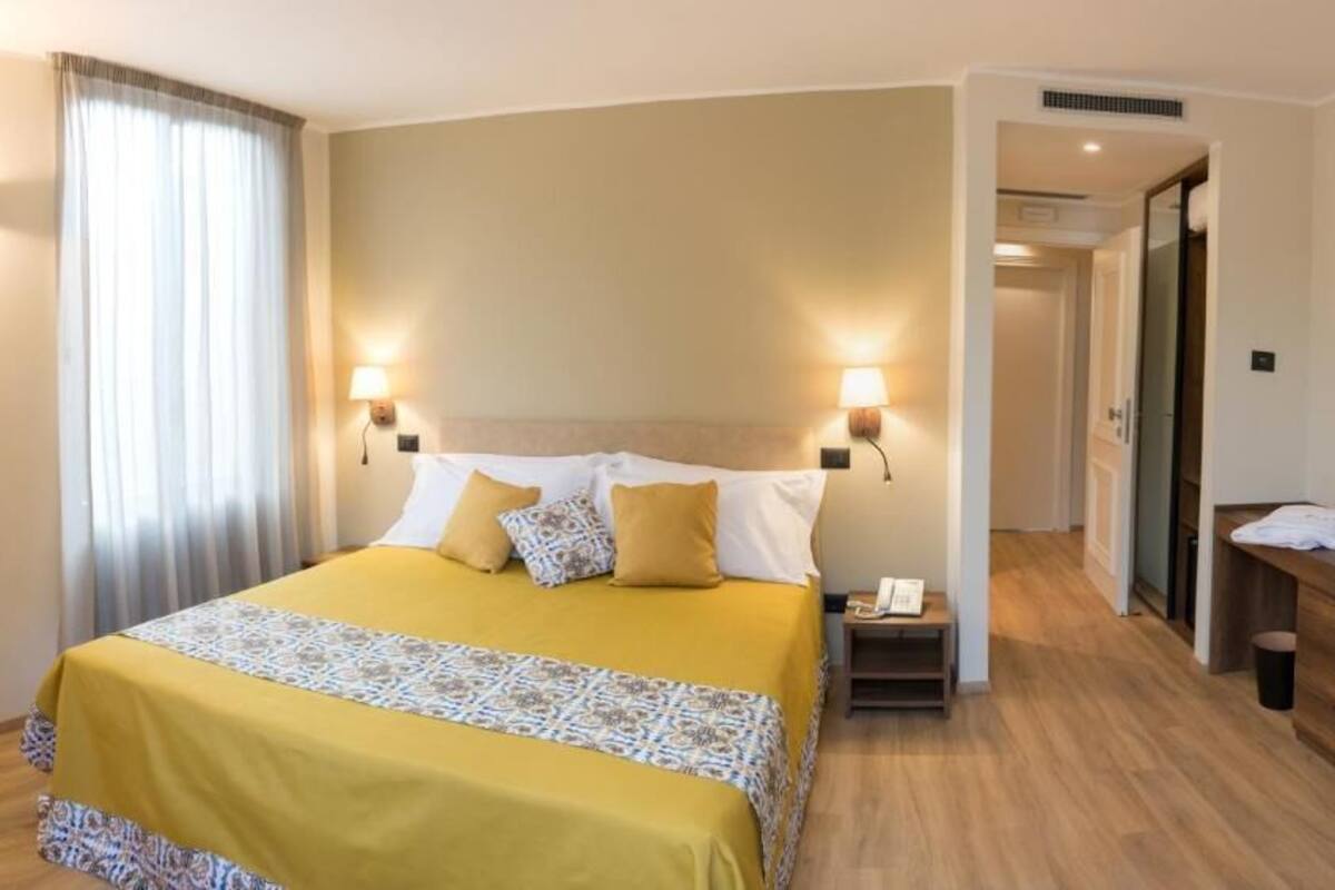 A hotel room with a bed, bedside table, desk, chair, and a phone.