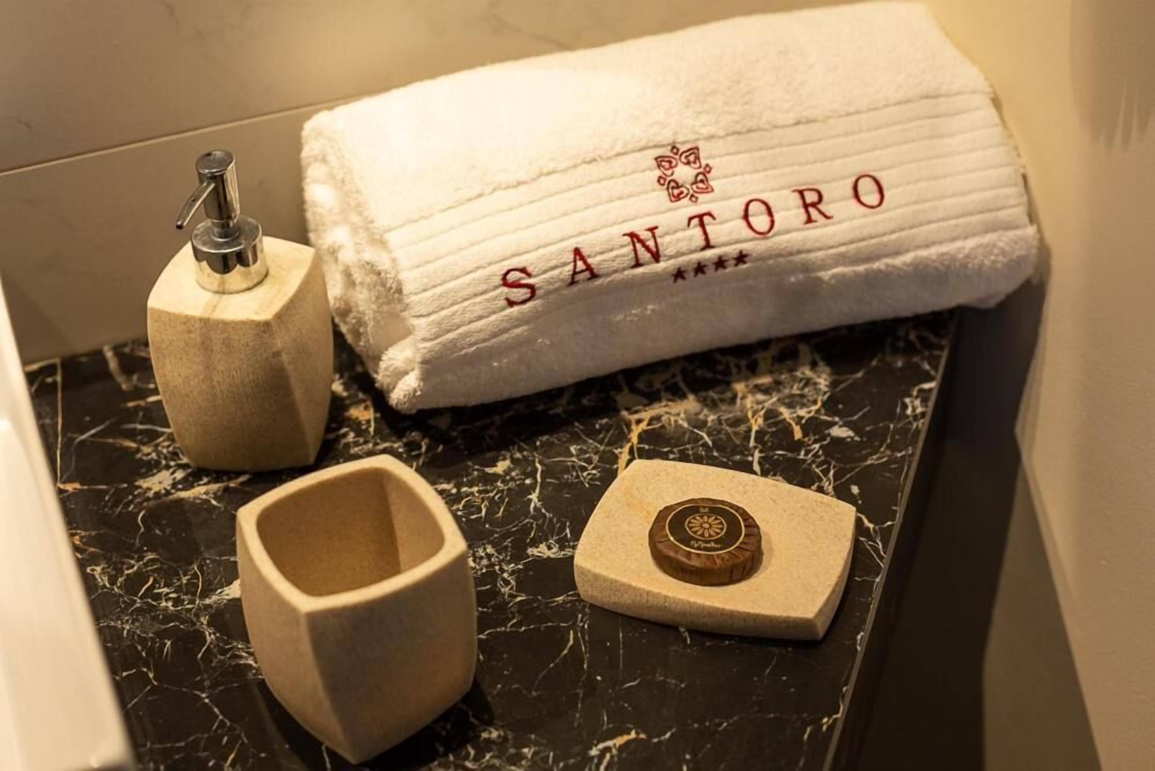 A bathroom with a marble countertop, a towel with 'SANTORO' embroidered on it, a soap dispenser, and a soap dish.