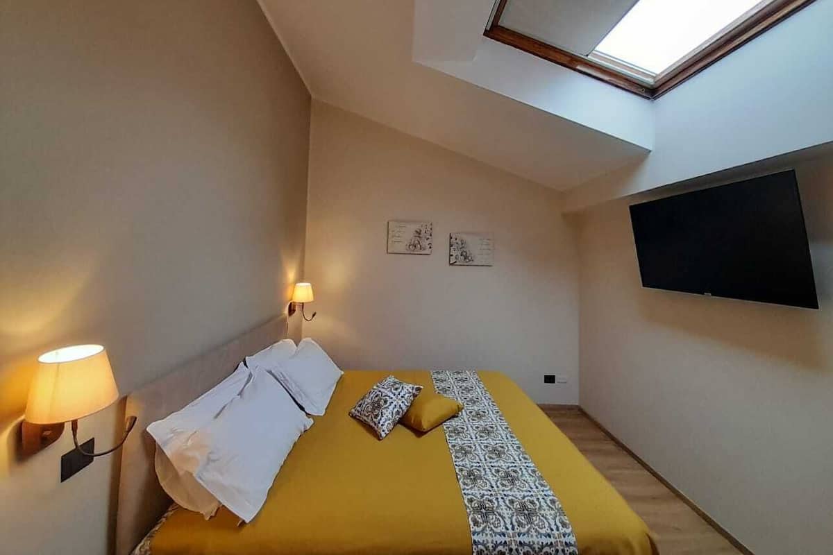 A bedroom with a bed, two wall-mounted lamps, a flat-screen TV, and a skylight.