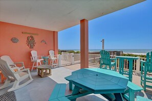 Un área de estar al aire libre cubierta con sillas y mesas, vista al océano y una pared de color melocotón con detalles decorativos.
