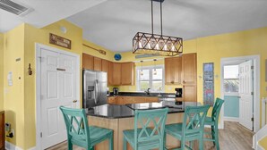 Una cocina con isla central, armarios de madera, refrigerador de acero inoxidable y sillas color turquesa.