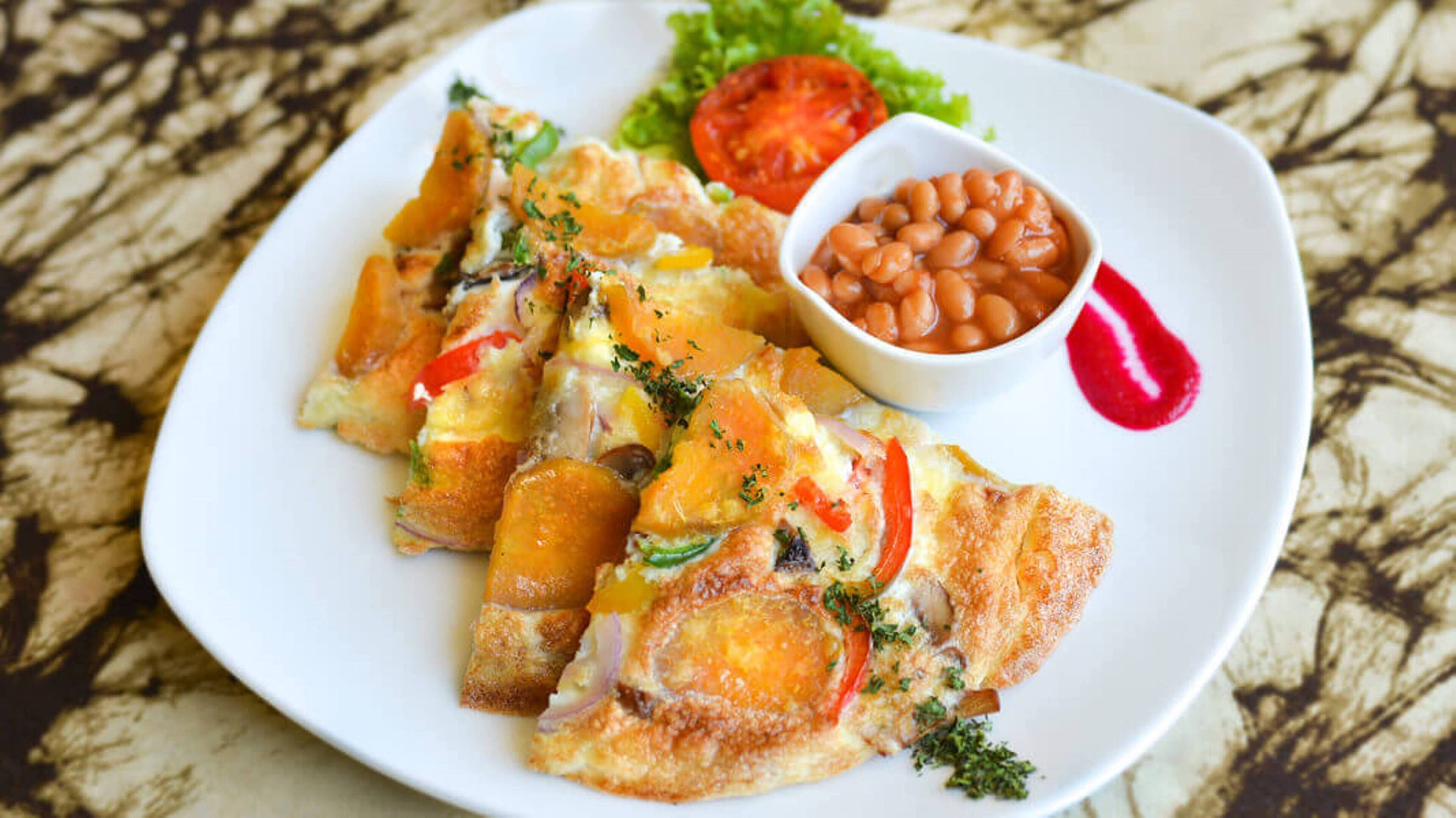Une assiette contenant un plat de poisson frit, une tranche de tomate et un bol de haricots.