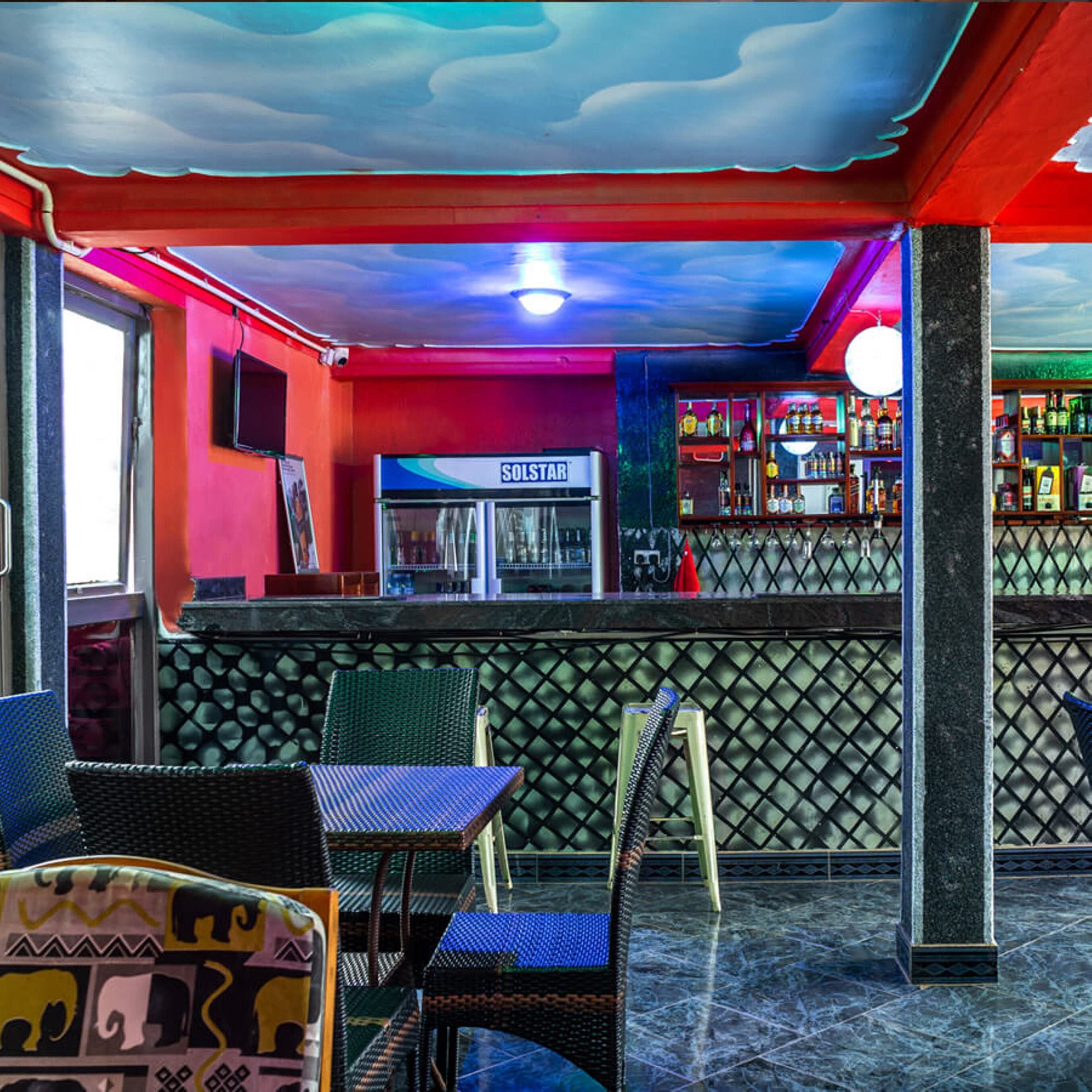 Un bar con techo rojo y azul, una barra con el rótulo 'SOLSTAR' y estanterías llenas de botellas.