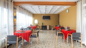 A conference room with multiple tables and chairs, a clock on the wall, and a television mounted on the wall. - Governors Hotel (Mukono)
