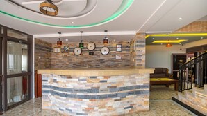 A reception area with a stone counter, clocks, and a staircase. - Governors Hotel (Mukono)