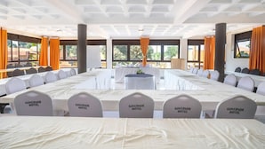 A conference room with long tables, white chairs, and orange curtains. - Governors Hotel (Mukono)