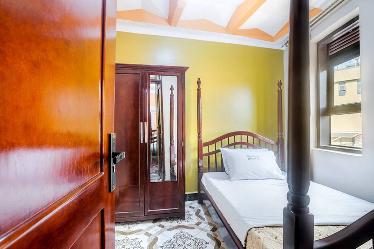 Un dormitorio con un armario de madera, una cama con almohada blanca y una ventana con persianas.