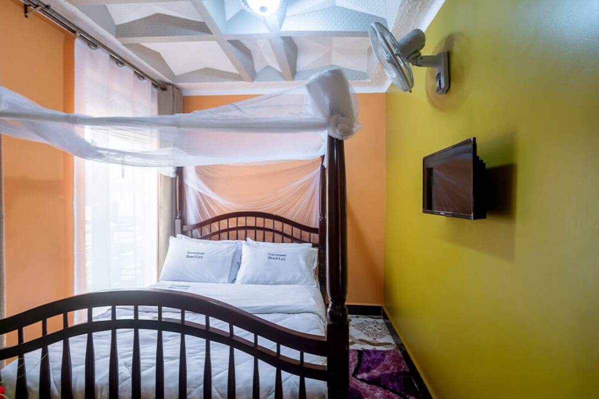Una habitación con una cama, un televisor montado en la pared y un ventanal con cortinas.