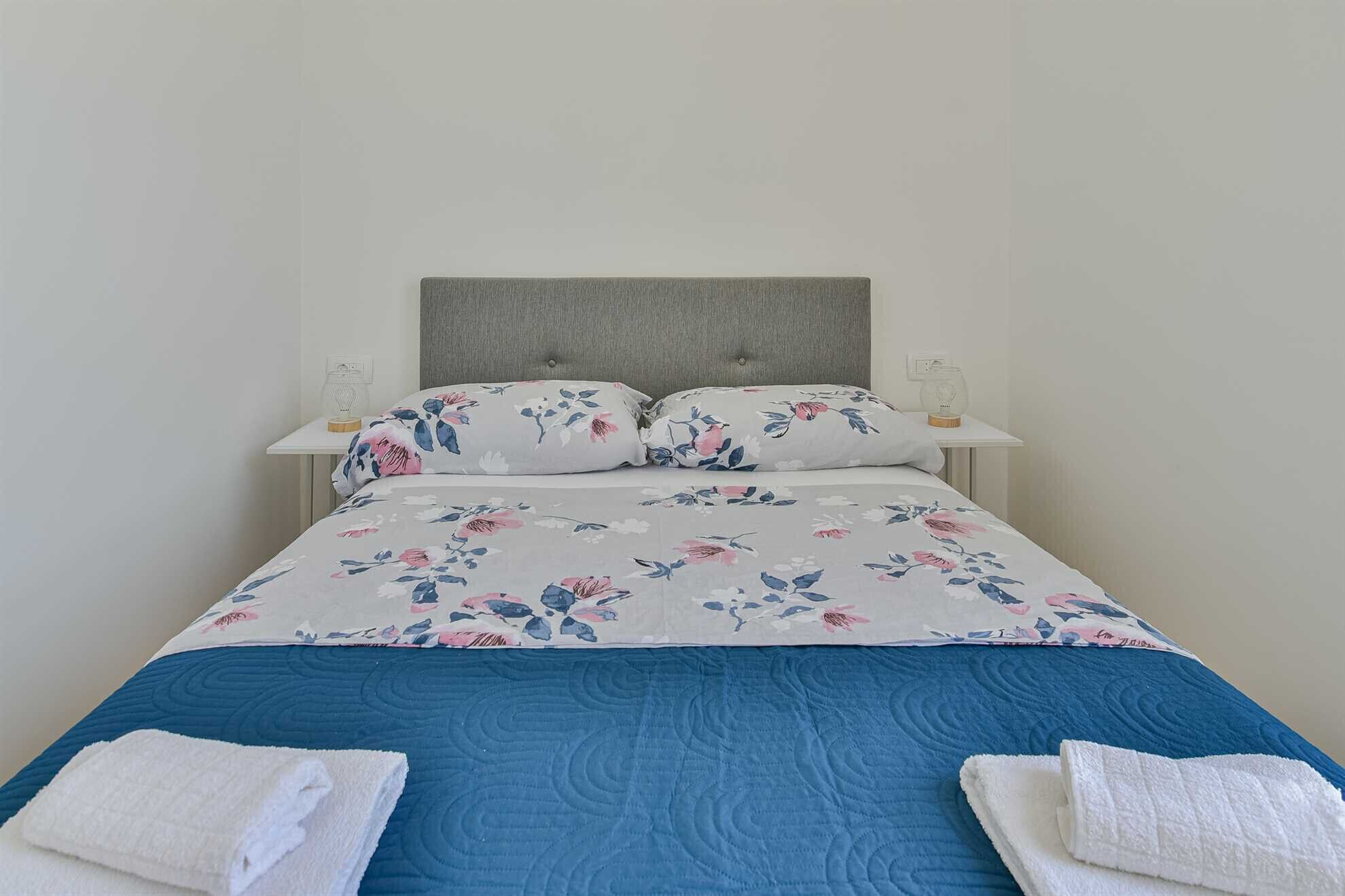 Un letto rifatto con copriletto floreale, due cuscini e due asciugamani piegati.