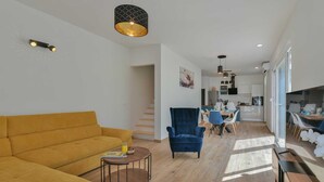 Un saló modern amb un sofà groc, un armari blau i una taula de centre rodona. Es pot veure una cuina al fons amb una zona de menjador.