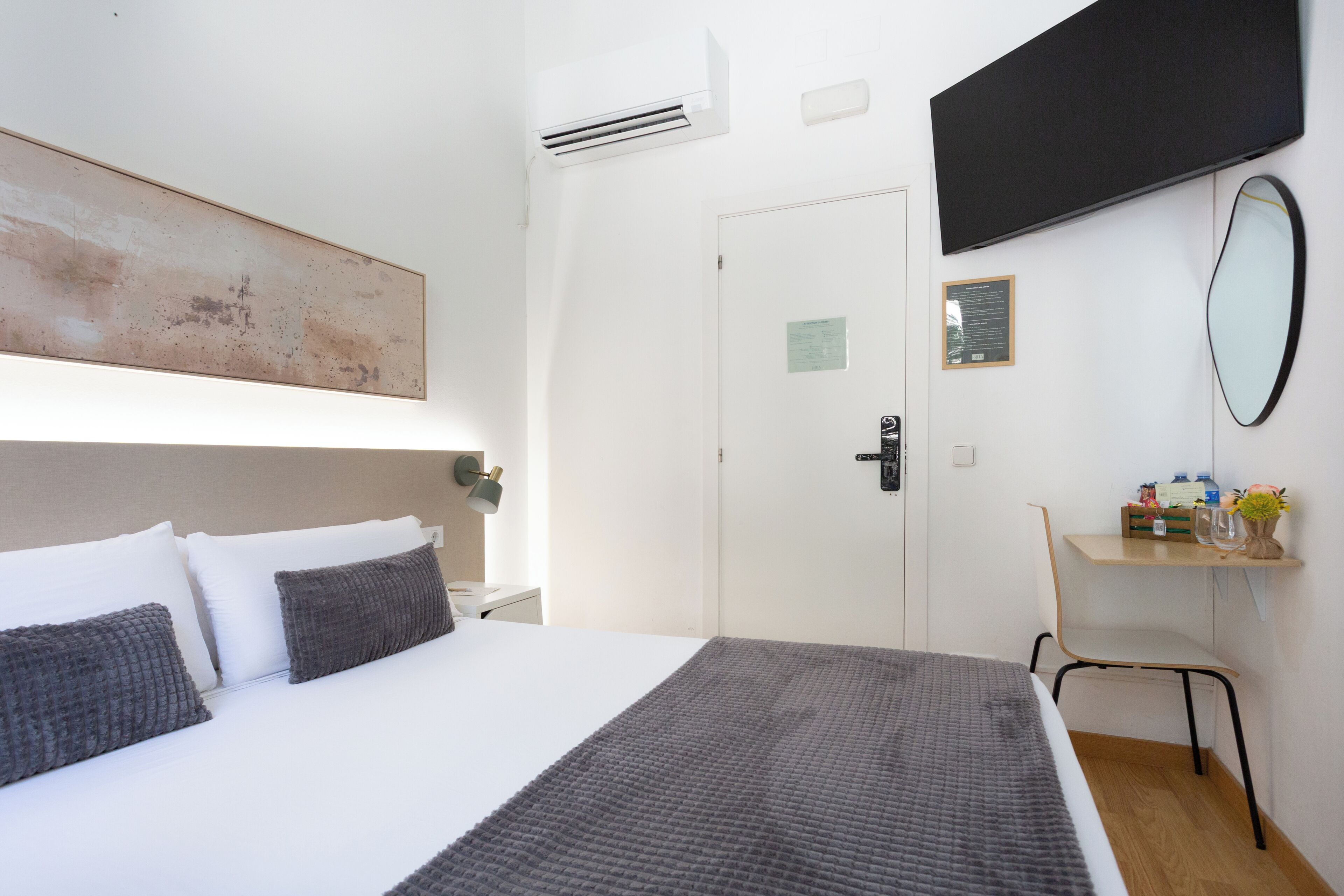 A hotel room with a bed, a desk, a chair, a flat-screen TV, and a wall-mounted mirror.