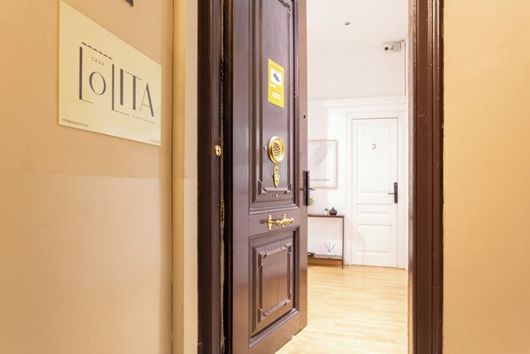 A wooden door with a brass handle and a plaque, a white door in the background, and a wooden floor. - Casa Lolita Guesthouse (Barcelona)