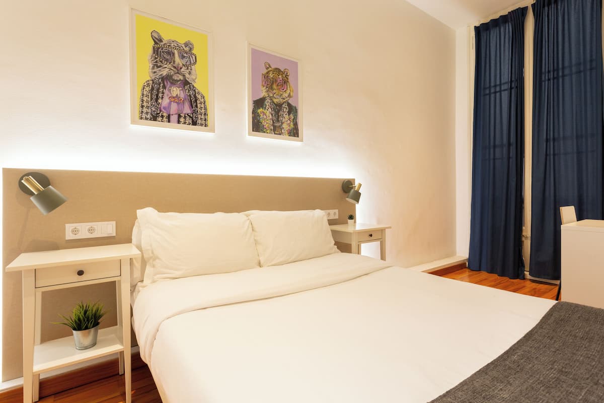 A neatly arranged bedroom with a bed, bedside tables, and a nightstand with a plant.