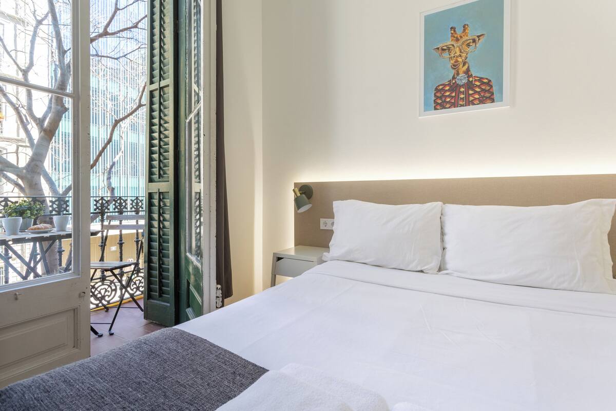 A hotel room with a bed, a nightstand, a painting, and a view of the outside balcony.