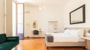 Een slaapkamer met een bed, een bureau, een stoel, een groene bank en een grote spiegel aan de muur.