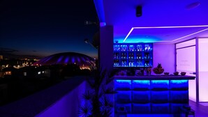 A modern bar area with a neon blue light, a large window, and a view of a stadium at dusk. - La Vie Villa Jelena with rooftop pool, Zadar county (Zadar)
