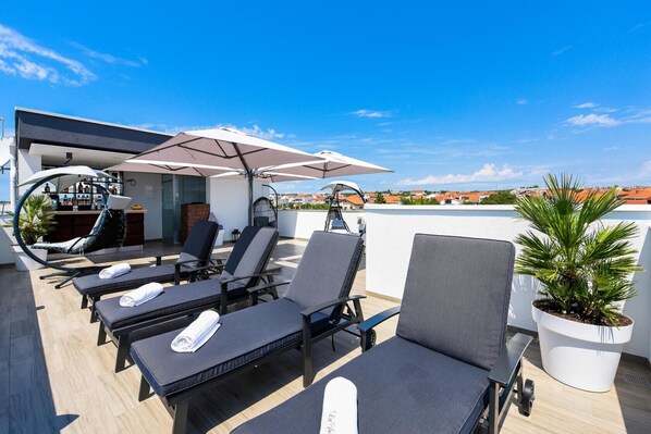 A rooftop terrace with sun loungers, a bar area, and a potted plant.