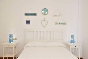 A bedroom with a white bed, two bedside tables, and wall decorations including a clock and signs saying "SWEET DREAMS," "ENJOY LIFE," and "I ♥ MARBELLA."