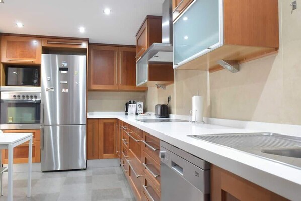 A modern kitchen with stainless steel appliances, wooden cabinets, and a white countertop.