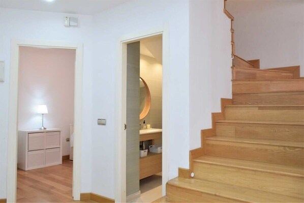 A staircase leading to a second floor, a small desk with a lamp, and a bathroom with a mirror and sink.