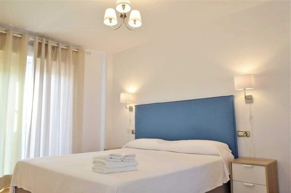 Ein Hotelzimmer mit einem großen Bett, zwei Nachttischlampen, einem Nachttisch und einem Fenster mit Vorhängen.