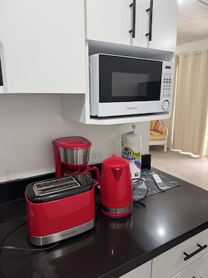 A kitchenette with a microwave, toaster, and coffee maker on a black countertop.