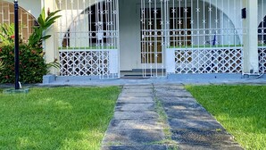 Un edificio con entrada porticada, un camino pavimentado que conduce a él y un césped bien cuidado.