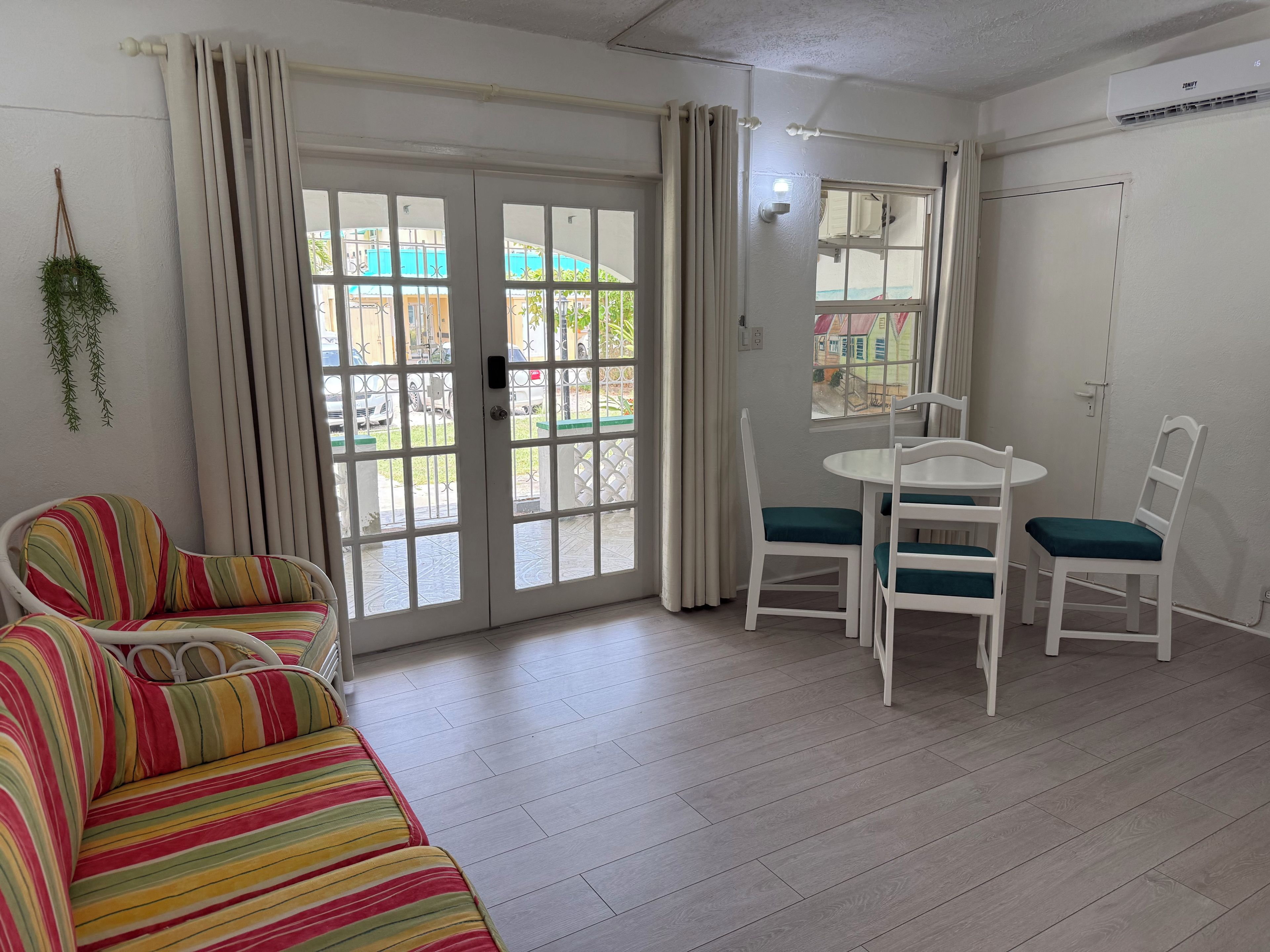 Une pièce avec un canapé à rayures, une table à manger avec des chaises, et une vue à travers une porte vitrée.