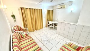 Una sala de estar con un sofá, una mesa de comedor con sillas, un ventilador de techo y una ventana con cortinas.