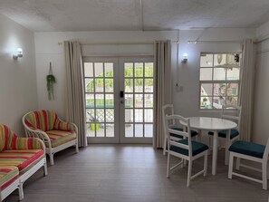 Une pièce comprenant une table à manger et des chaises, un canapé et une vue sur l’extérieur, visible à travers une porte vitrée.