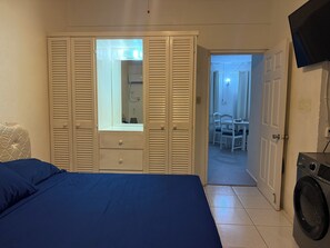 Quarto com cama, armário com espelho, máquina de lavar roupa e área de refeições com cadeiras e mesa.
