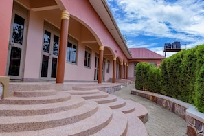 A building with a pink facade, multiple windows, and a set of curved stone steps leading to the entrance. - Mujo Suites Hotel (Sembabule)