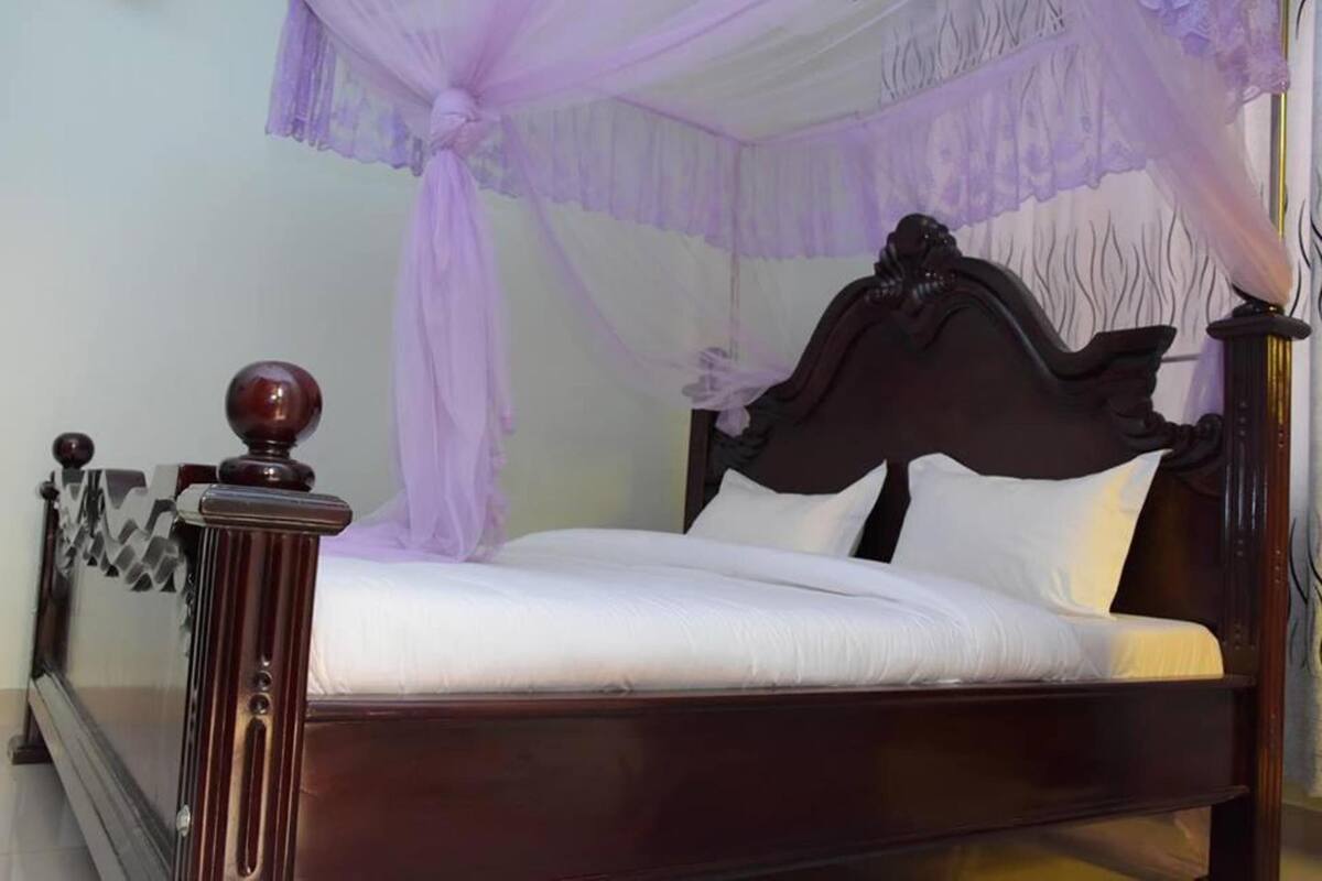 A bed with a dark wooden frame and a white mattress, covered by a purple canopy.