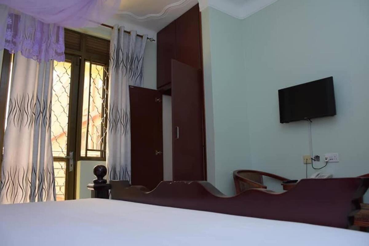 A hotel room with a bed, a television mounted on the wall, a wooden chair, and a wardrobe.