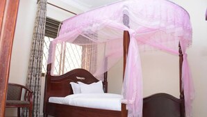 A four-poster bed with a canopy, a wooden headboard, and a white mattress. - Day 2 Day Prime Hotel (Kampala)